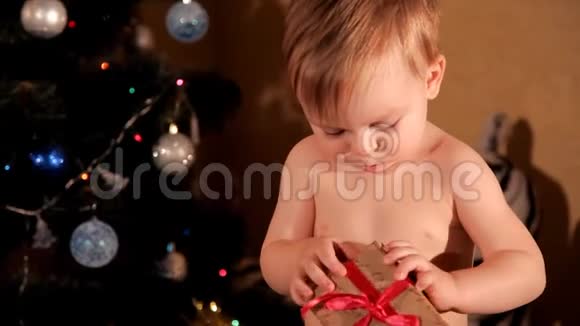 一个小孩正试图在圣诞树附近打开的新年礼物视频的预览图