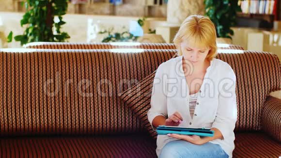 穿夏季衬衫的女士在酒店大堂使用平板电脑视频的预览图
