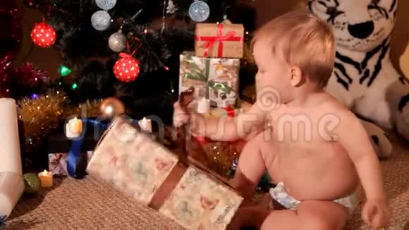 一个小孩正试图在圣诞树附近打开的新年礼物视频的预览图