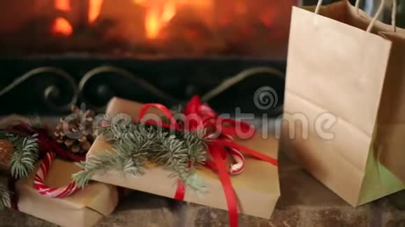 圣诞礼物装饰着云杉树枝球果丝带放在壁炉旁温暖的原木着火了圣诞节视频的预览图