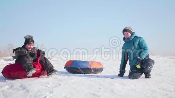 两个孩子骑在雪橇上的雪山上孩子们坐在山顶上体育和户外活动视频的预览图