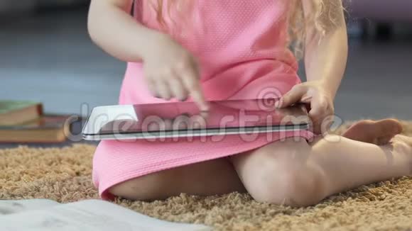 小卷发女孩坐在地毯上在平板电脑上滚动教育应用程序视频的预览图