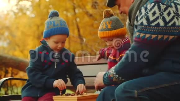 孙子们正在秋天公园的长椅上和爷爷下棋视频的预览图
