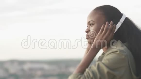 美丽的年轻非洲女孩正在通过耳机听音乐侧面特写户外画像视频的预览图