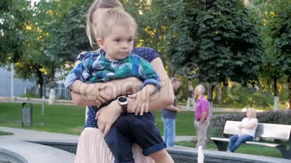 慢镜头视频快乐微笑的母亲拥抱和抱着她2岁的小男孩在公园视频的预览图