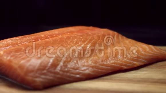 一块新鲜的生的红色的鱼放在一木制的棕色切割板上隔离在黑色的背景上美丽的鲑鱼片视频的预览图