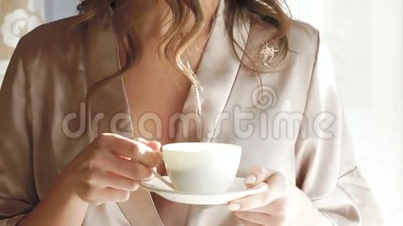 穿睡衣的漂亮女孩在窗户附近喝了一杯咖啡慢慢地视频的预览图