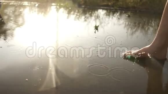 光着脚的近处穿过一个水坑水映出夕阳的光芒滴下雨点夏季视频的预览图