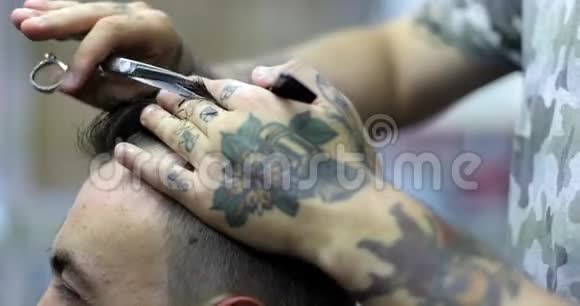 理发师手上有纹身用梳子和剪刀剪头发视频的预览图