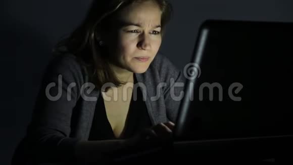 勤劳的女人在黑暗的办公室里用眼镜在笔记本电脑上工作视频的预览图