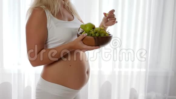 孕妇健康食品肚子大的女性在窗户附近吃葡萄拿着木盘视频的预览图