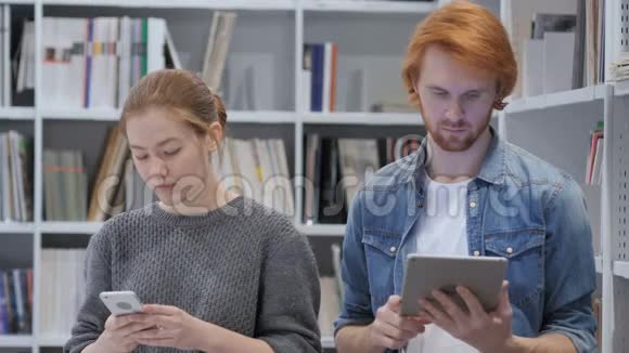 红发男子使用平板电脑妇女使用办公室智能手机视频的预览图