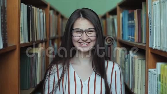 图书馆里年轻漂亮女孩的肖像女学生在书架之间的许多书中学习视频的预览图