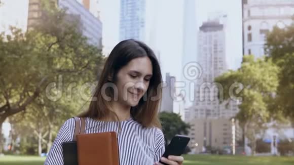 年轻的快乐女商人站在美国纽约金融区用智能手机作为移动办公室视频的预览图