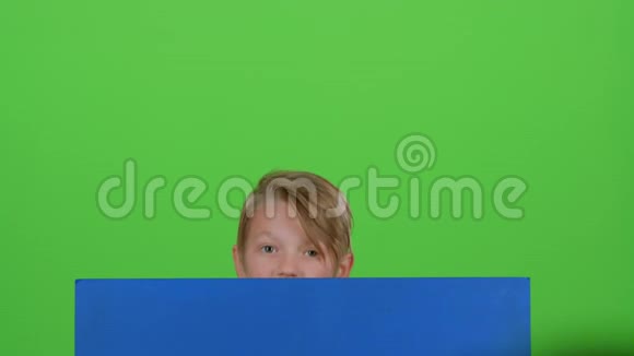 小男孩从一张蓝色的海报后面出现看着他的表演就像又躲起来一样绿色屏幕视频的预览图