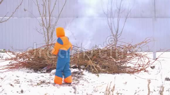 快乐村的孩子们穿着明亮温暖的衣服在花园里的灰色篱笆上从树枝上围着篝火玩孩子们哈视频的预览图