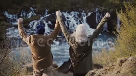 后景年轻时尚夫妇举手和感觉快乐自由附近的瀑布在冰岛视频的预览图