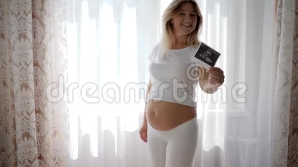 母亲摸了摸他赤裸的怀孕腹部并在相机上显示了婴儿超声波扫描的快照视频的预览图