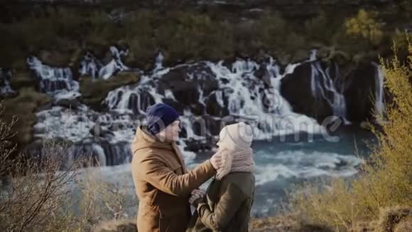 年轻的旅行夫妇在冰岛瀑布附近浪漫约会男人和女人拥抱自然视频的预览图