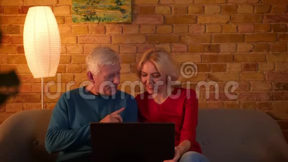 在舒适的公寓里高级幸福夫妇用笔记本电脑坐在沙发上的特写镜头视频的预览图