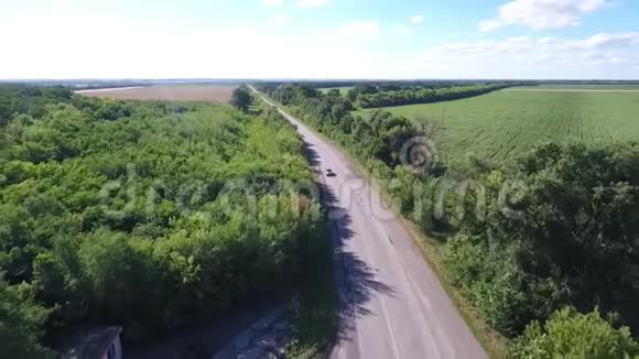 灰色的汽车在树木和田野之间快速地沿着道路行驶空中射击视频的预览图