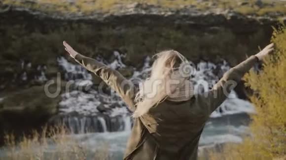 自由年轻的旅行妇女在冰岛看瀑布举起双手感到快乐视频的预览图