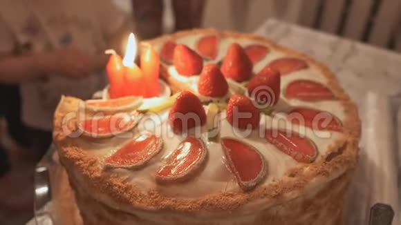 一只雌性手在用草莓和水果装饰的蛋糕上点燃蜡烛生日派对视频的预览图