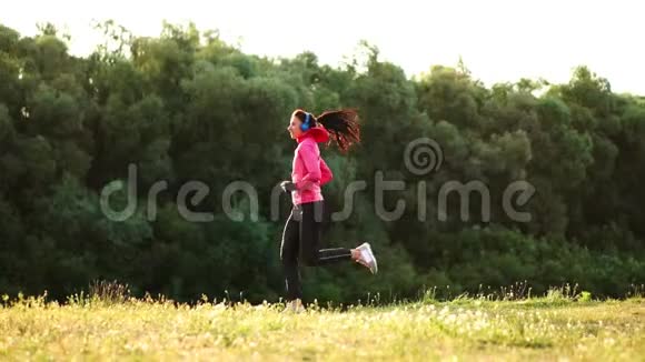 那个女孩在公园的日落时分沿着池塘跑步用耳机听音乐视频的预览图