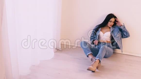 穿着牛仔裤西装坐在地板上的布鲁内特女孩视频的预览图