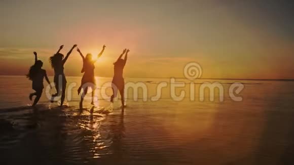 五个女孩组成的小组跑到水里在日落的海滩上庆祝海滩派对太阳耀斑慢动作视频的预览图