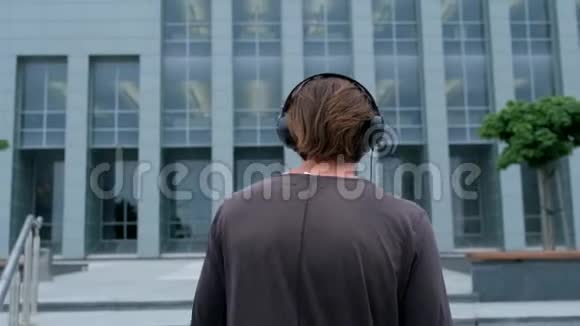自由职业者步行在大城市工作与笔记本电脑手机摄像头和听音乐通过耳机视频的预览图