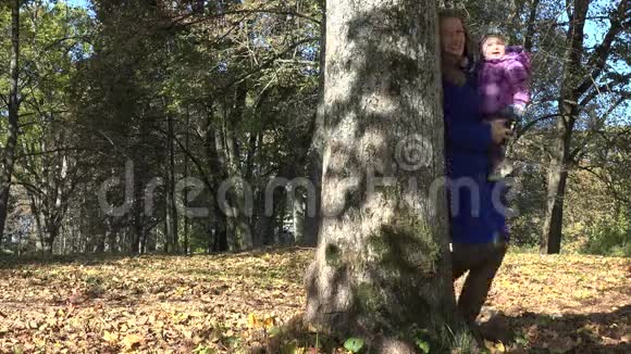 母亲带着小女儿躲在秋天公园的树后4K视频的预览图