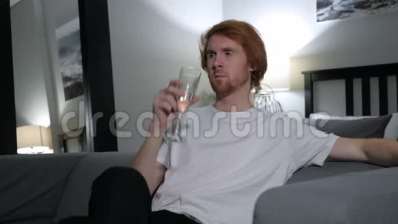 放松的红发男子喝香槟酒坐在沙发上视频的预览图