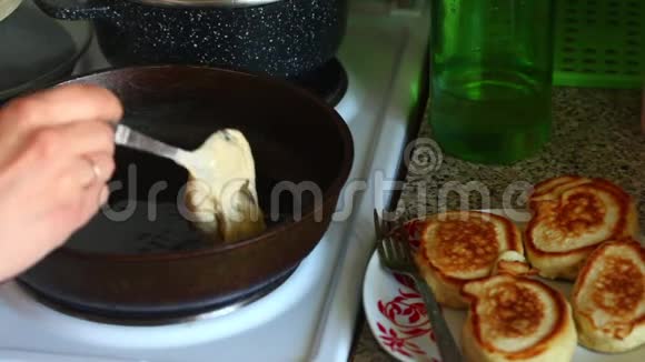 女人把面团放在热煎锅上盘子旁边是煮熟的煎饼准备煎饼视频的预览图