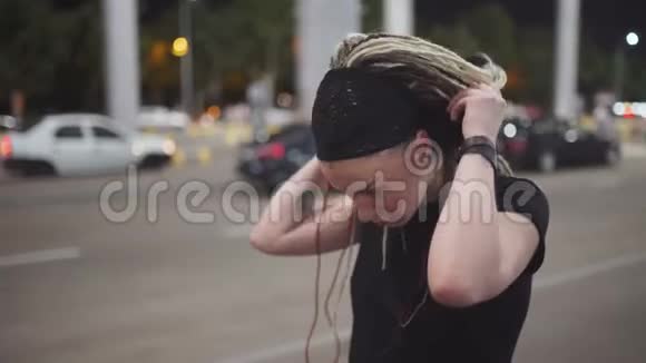 年轻有魅力的女人戴着恐惧症用智能手机在耳机上听音乐晚上在街上视频的预览图