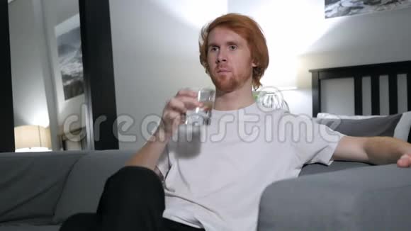 坐在沙发上喝水的男人视频的预览图