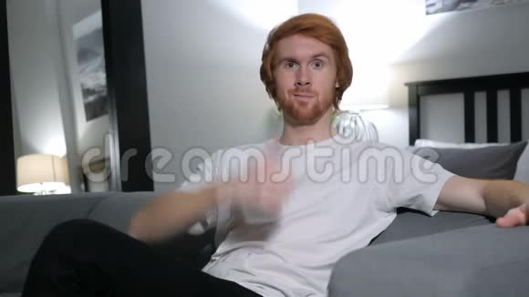 坐在卧室沙发上的红发男人竖起大拇指视频的预览图