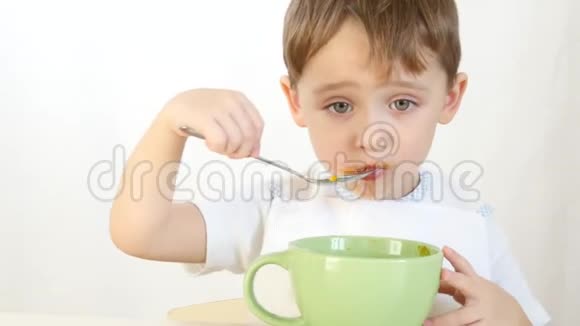 孩子高兴地用勺子从盘子里吃汤特写运动相机滑块一个男孩坐在桌子旁吃东西视频的预览图