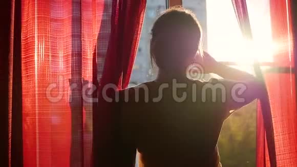 女孩打开红色的窗帘玩太阳光线女孩的剪影视频的预览图