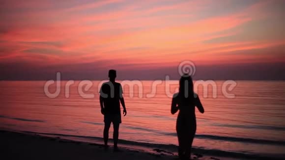 一对夫妇在令人惊叹的日落中在海滩上拍照的剪影高清高清视频的预览图
