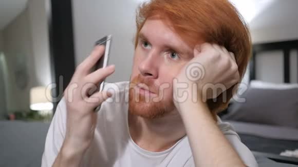 坐着红发男人在智能手机上聊天视频的预览图