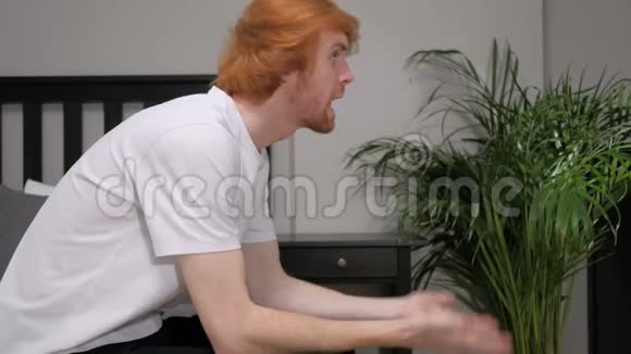 愤怒的红头发男人坐在床边视频的预览图