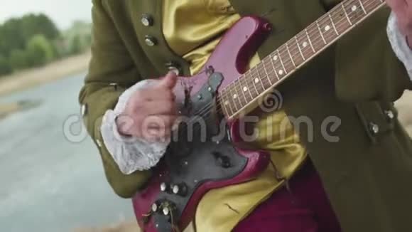 为一个穿着洛可可式老式服装在枯草上演奏的紫色电吉他的男人靠近视频的预览图