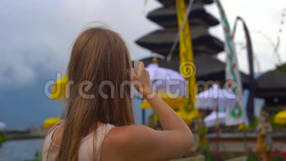 一名年轻女子在布拉塔纳湖上的PuraUlunDanu神庙用手机缓慢拍摄视频的预览图