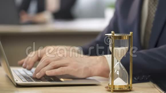 穿西装的人在办公室用笔记本电脑工作沙漏站在桌子上时间视频的预览图