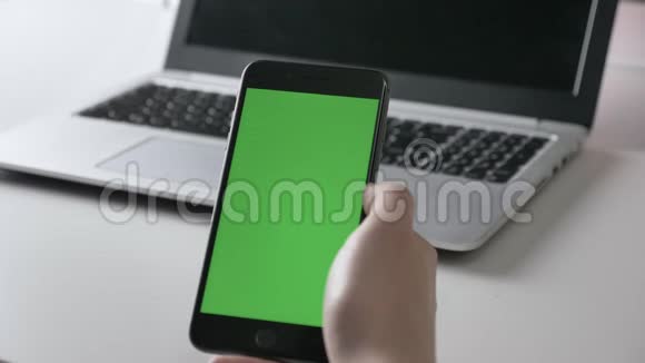 男人双手握着一个黑色的智能手机敲击手势绿色屏幕色度概念笔记本电脑背景60fps视频的预览图