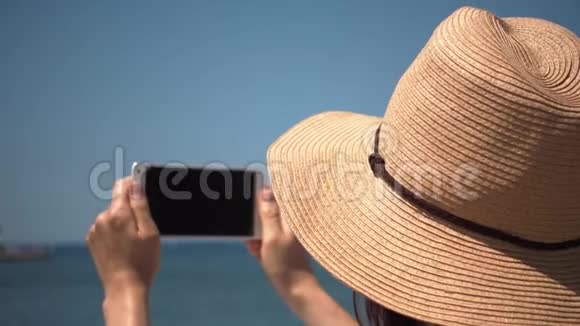 戴帽子的女人在海滩上用手机拍海视频的预览图