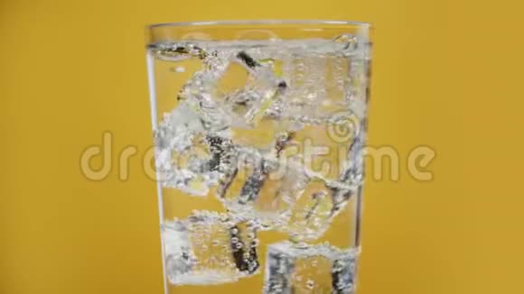 盛满气泡水的玻璃杯冰块黄色背景透明的泡沫饮料视频的预览图