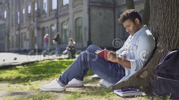 多种族年轻人坐在树下读有趣的书书虫视频的预览图