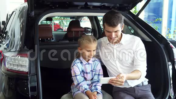 一位带着女儿的年轻父亲在汽车背景上自拍视频的预览图